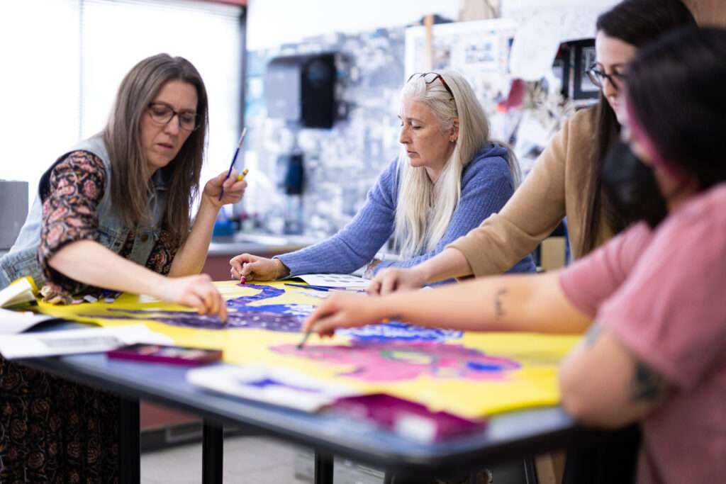 Educators sitting at table in a classroom working on an art project together