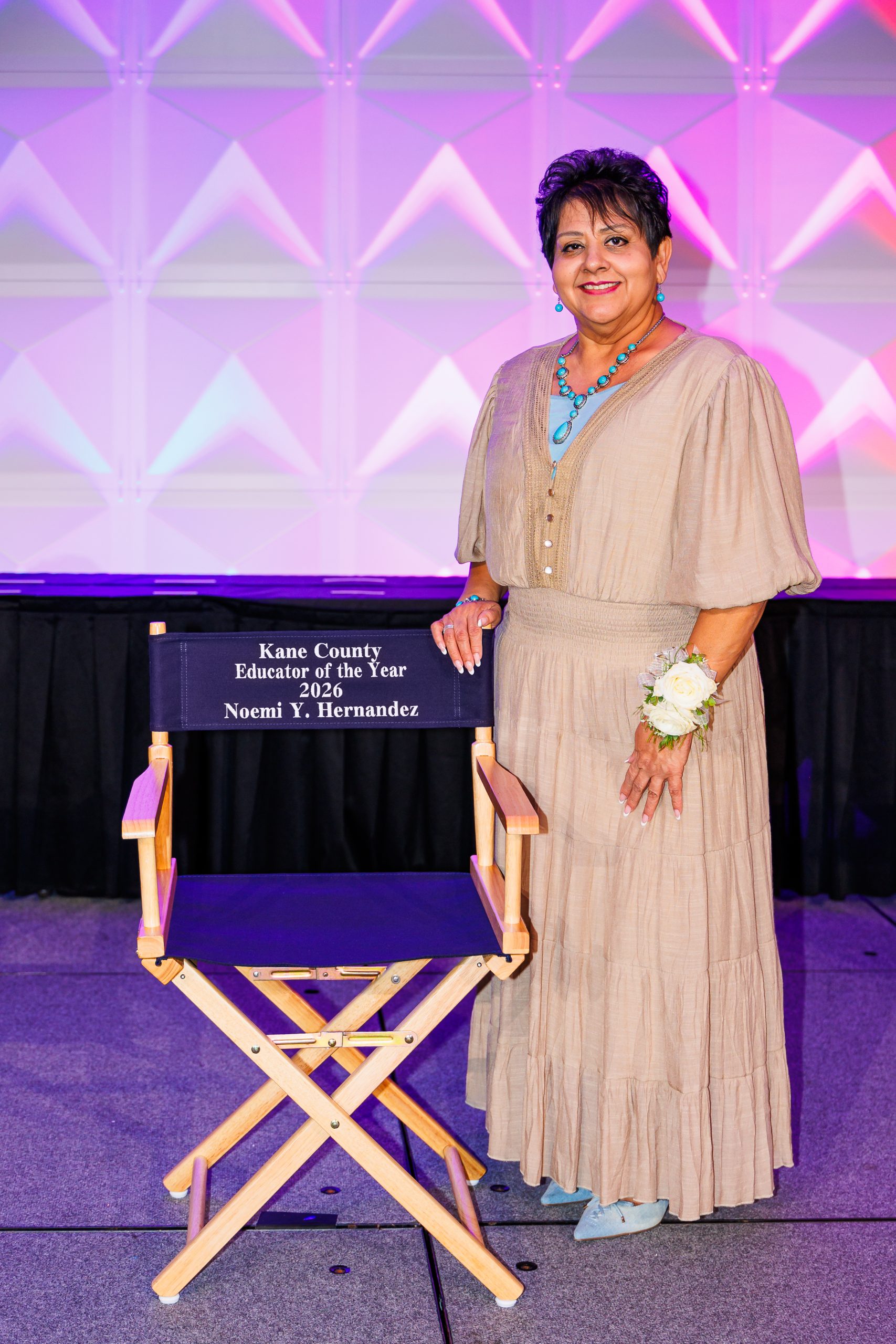 Educator posing on stage next to director's chair