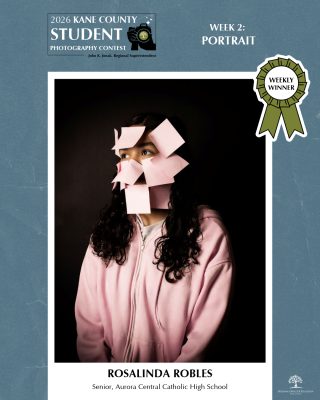 Portrait of a person dressed in a pink hoodie, face partially hidden by several pink sticky notes, looking to the side.