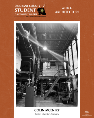 Black and white image of a boiler room filled with pipes, a metal staircase and a bright overhead light