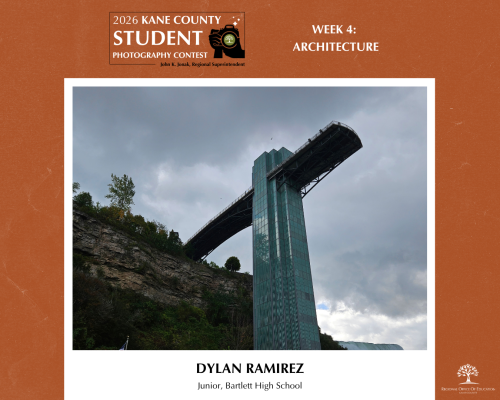 Tall modern glass tower extends horizontally over a cliff under a cloudy sky.