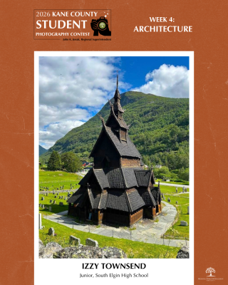 Historic wooden stave church with intricate tiered roofs set against green mountains and a partly cloudy sky